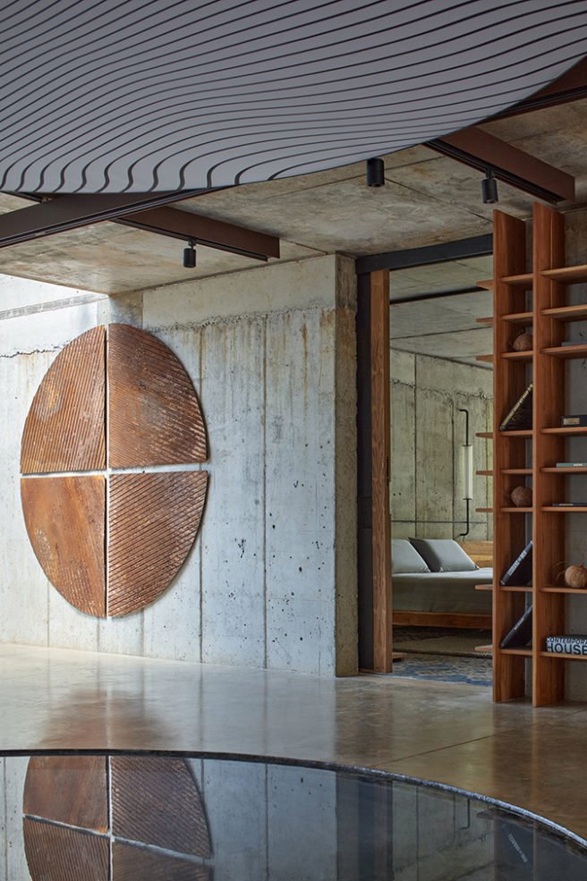 Escultura de acero en pared sobre hormigón con estantería y pierta hacia dormitorio en madera
