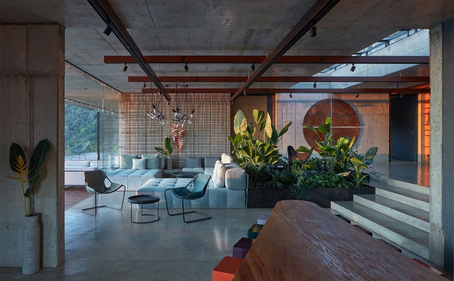 Salón con sofás mullidos y modulares en blanco y gris, amplia jardinera central junto a escaleras de hormigón