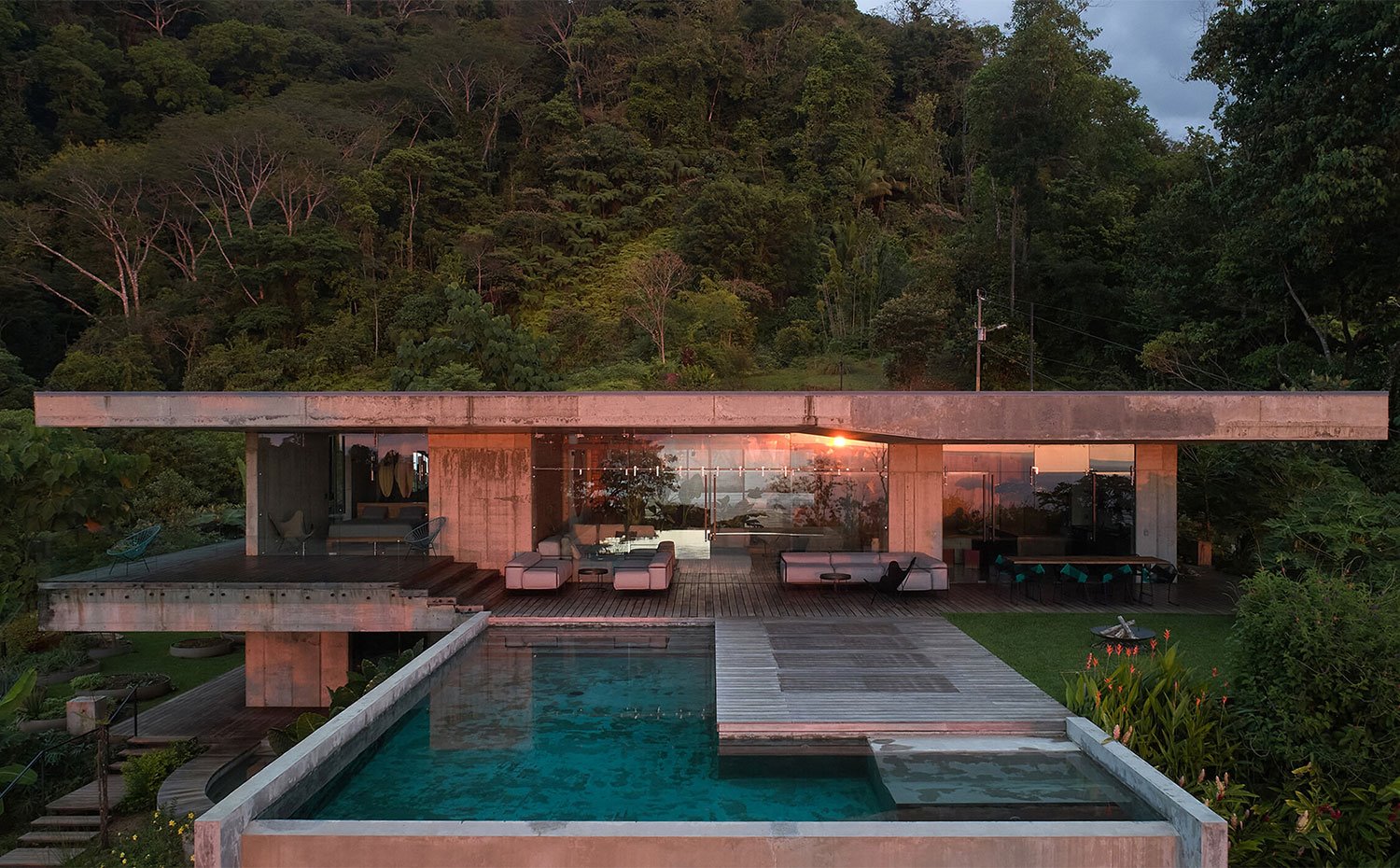 Vista exterior al atardecer desde la piscina con estructura de hormigón y cerramientos de cristal