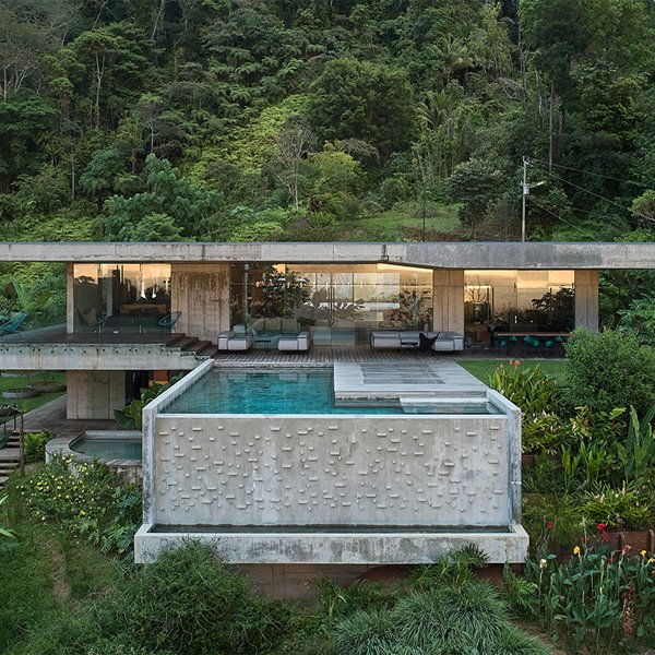 Vista general de la vivienda con gran piscina junto a terraza y escaleras de madera entre densa vegetación