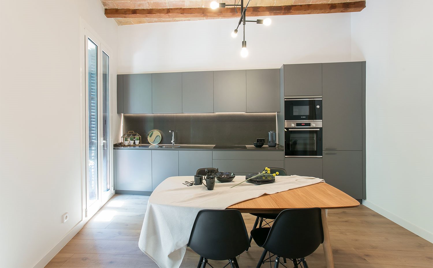 Cocina abierta en gris ante mesa de comedor de madera y sillas negras