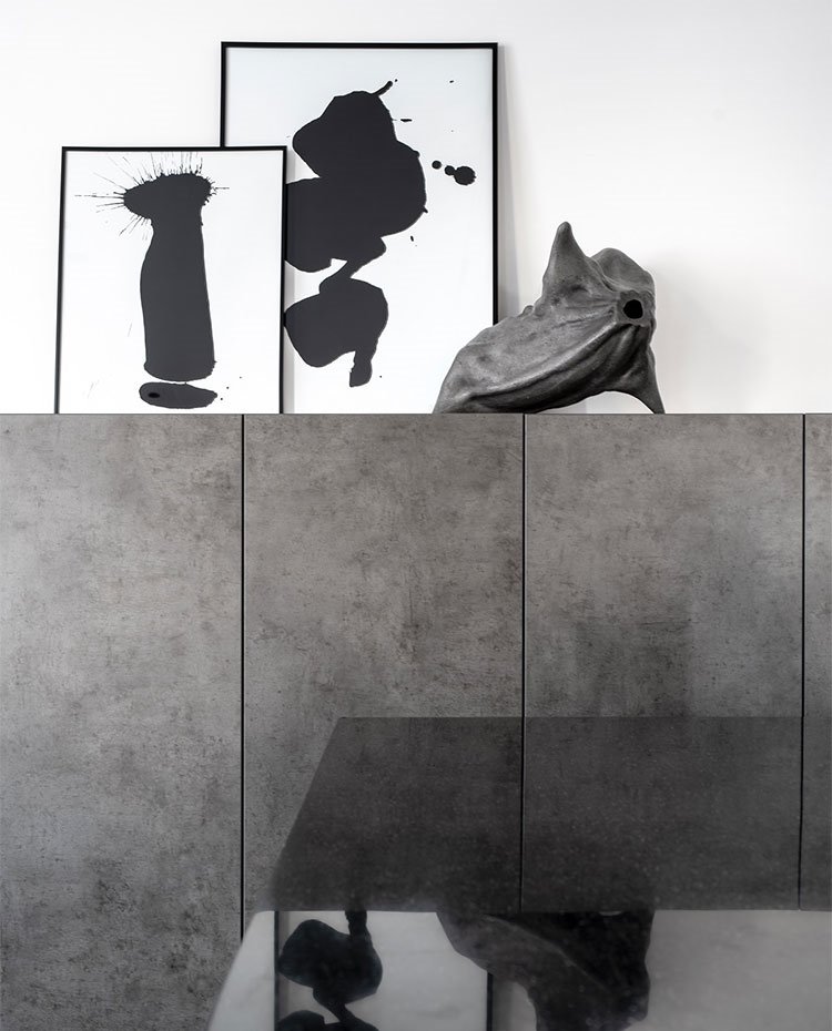 Detalle de cuadros y escultura sobre mueble contenedor en gris junto a zona de cocina con encimera de granito en negro.