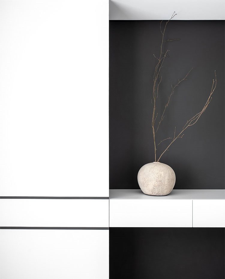 Detalle mobiliario en blanco sobre pared en negro con estante suspendido y jarrón de formas circulares
