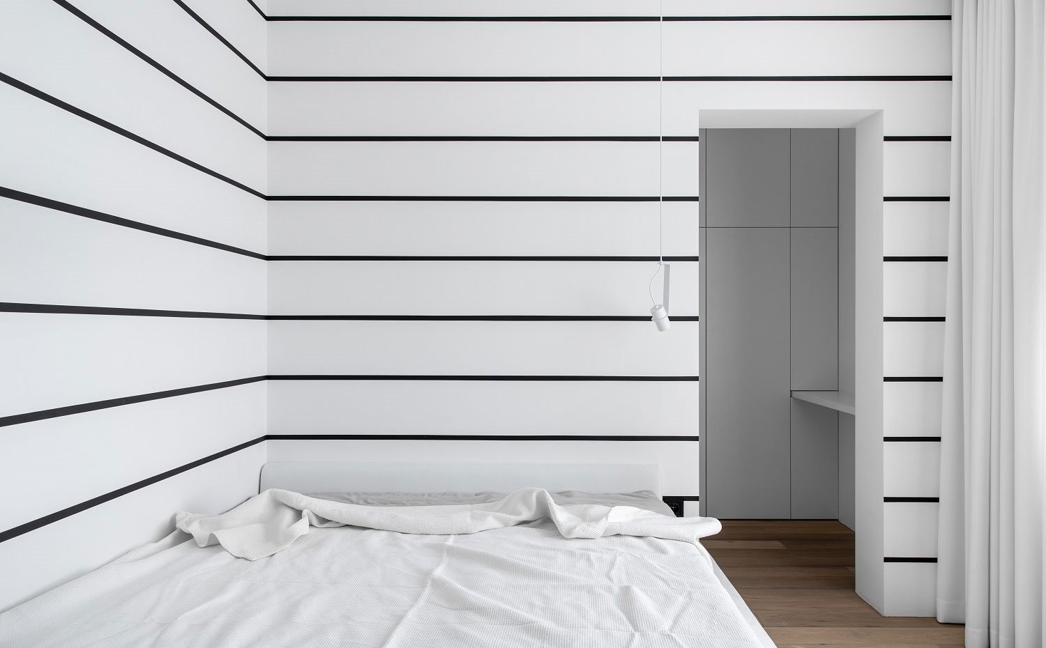 Dormitorio con luminaria puntual suspendida, detalle de pared a rayas horizontales negras 
