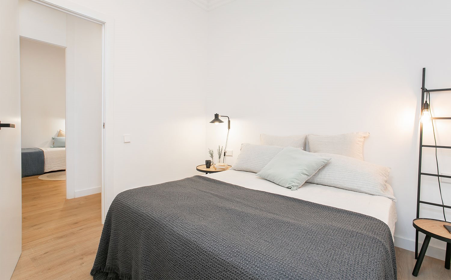 Dormitorio con mobiliario e ilumación en acabado negro, suelo de madera, puertas y paredes en blanco