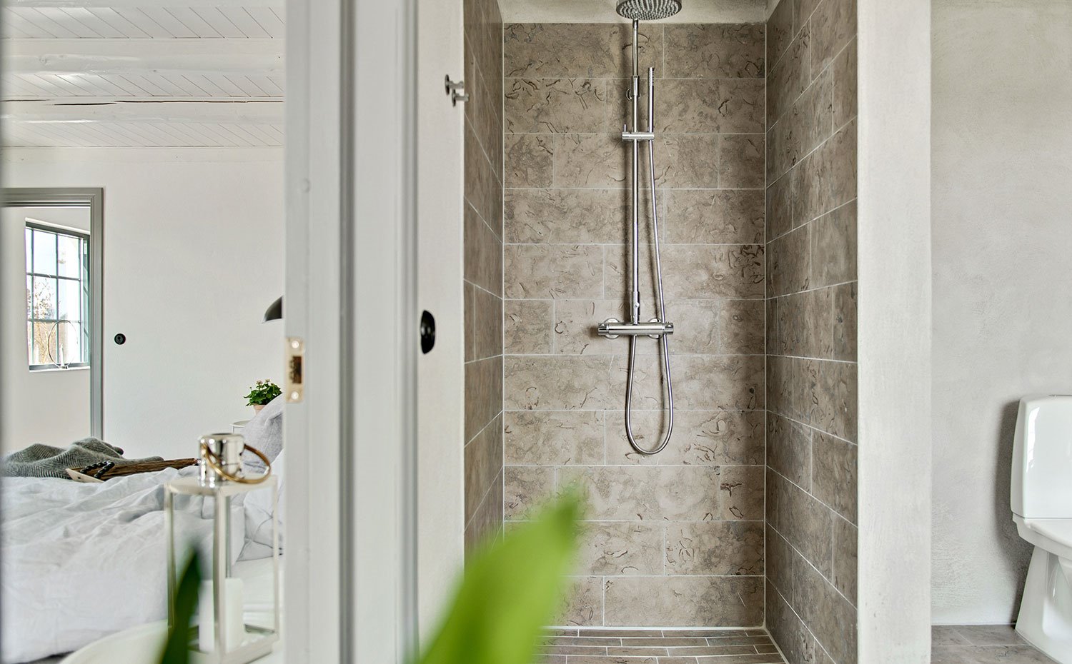 Ducha con revestimiento en tonos grisáceos junto a dormitorio y separada por un tabique con el resto del cuarto de baño
