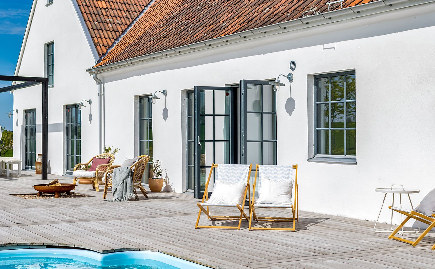 Exterior de vivienda junto a piscina con hamacas de madera, fachada en blanco con techos de tejas