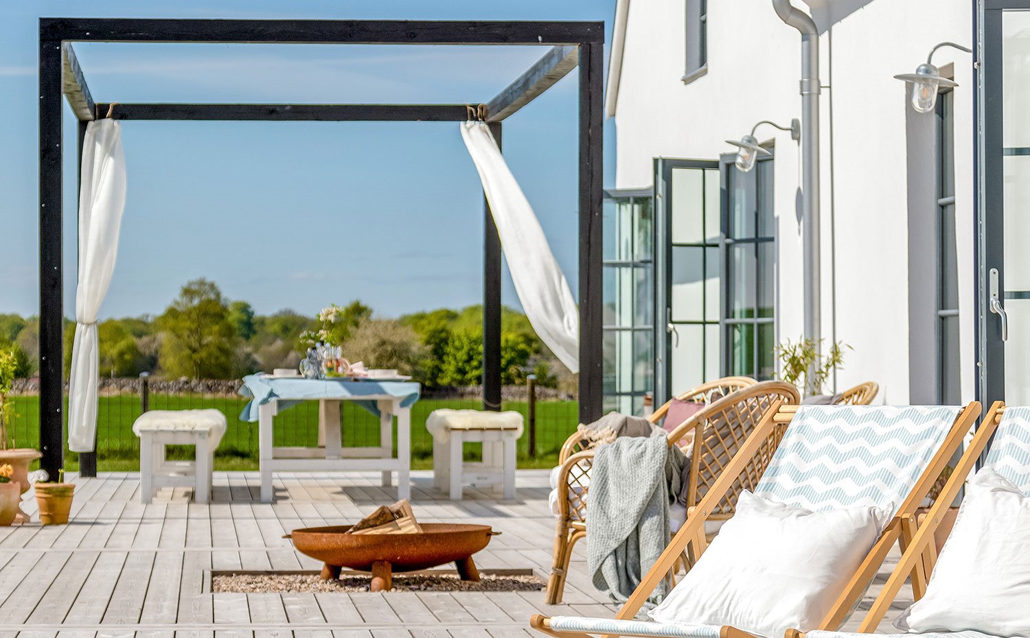Terraza con mobiliario exterior en madera y fibras naturales, entarimado de madera y estructura metálica a modo de pérgola