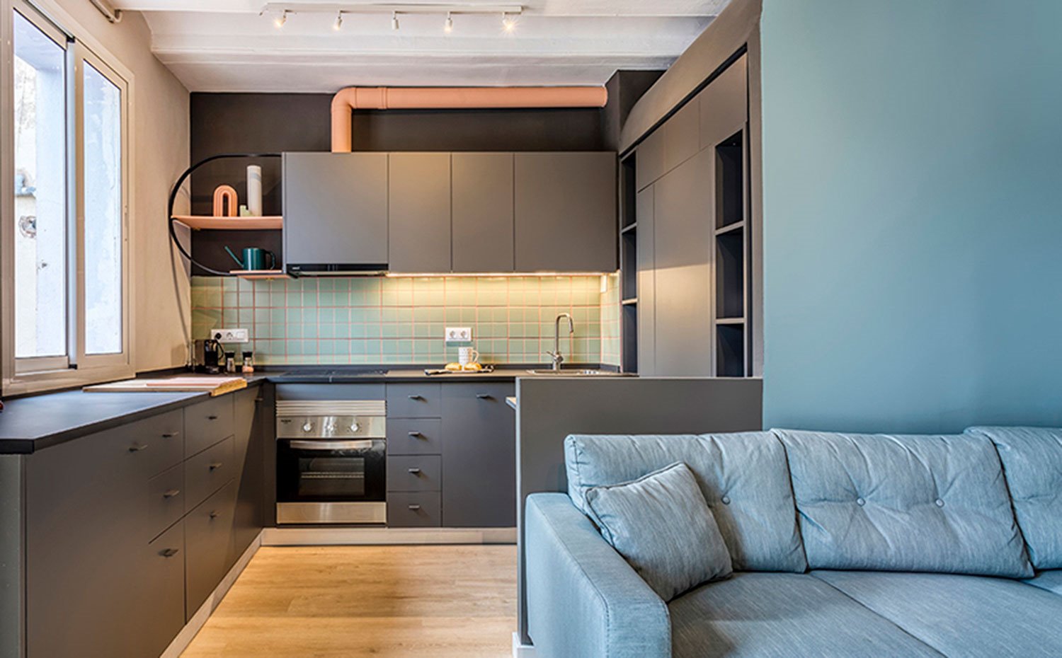 Cocina abierta con disposición en L y mobiliario en gris, revestimiento en verde turquesa 