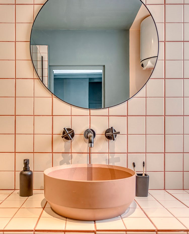 Tocador cuarto de baño con lavamanos exento sobre baldosas de tonos crudos y juntas en rosa salmón, complementos y grifería en gris