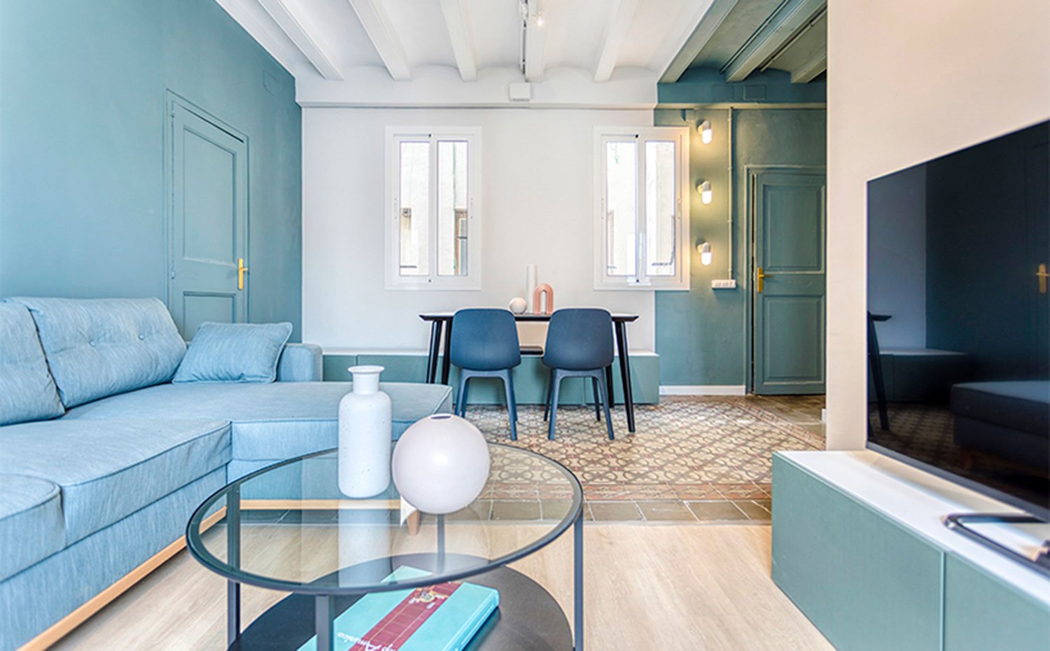 Zona de salón revestida de madera y comedor con suelo hidráulico, mesa de centro de cristal