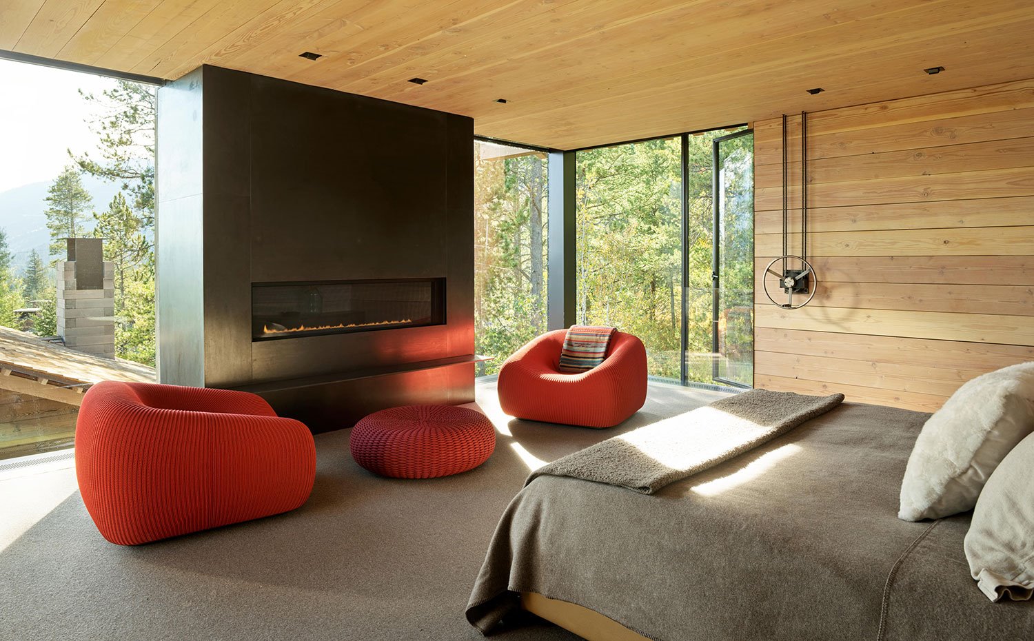 Dormitorio con chimienea, butacas y poufs en rojo, suelo enmoquetado, techos y paredes de madera