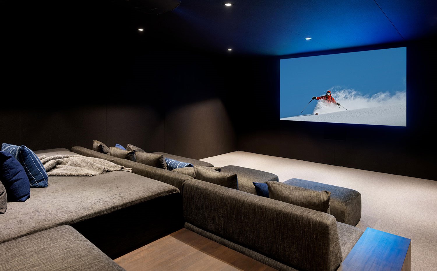 Sala de cine con gran pantalla de visionado y sofás en gris
