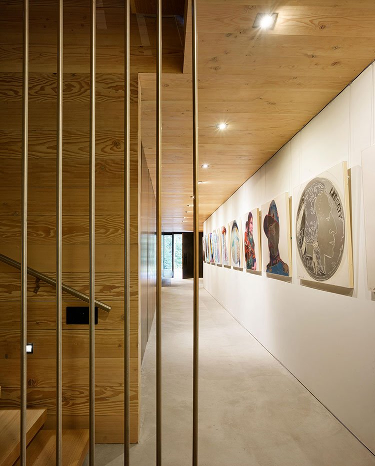 Zona de paso con suelo enmoquetado, paredes y techo revestido de madera y frente de pared con sucesión de cuadros 