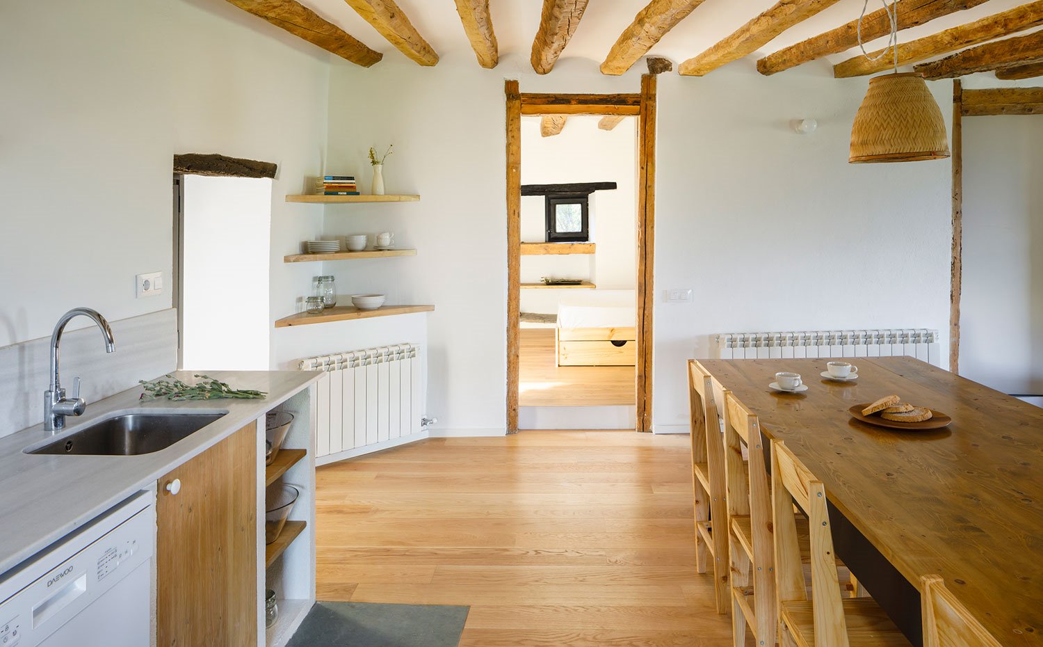 Cocina con encimera gris claro y muebles de madera, mesa y sillas de comedor de madera, marcos de puertas y vigas de madera