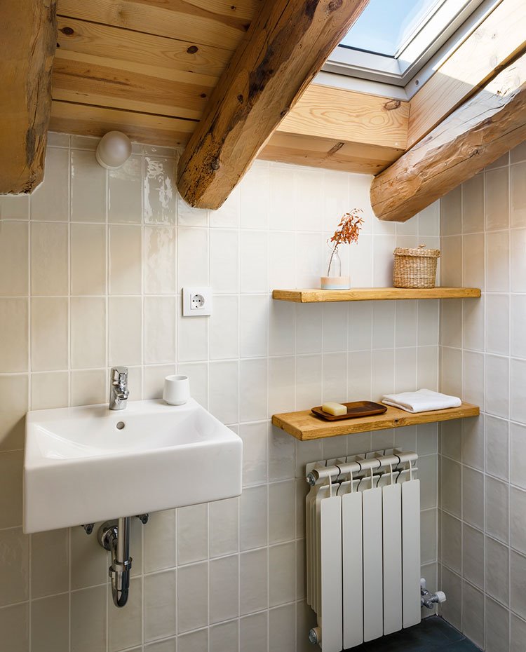 Cuarto de baño con lucernario bajo cubierta, techo de madera y revestimeinto en gris claro