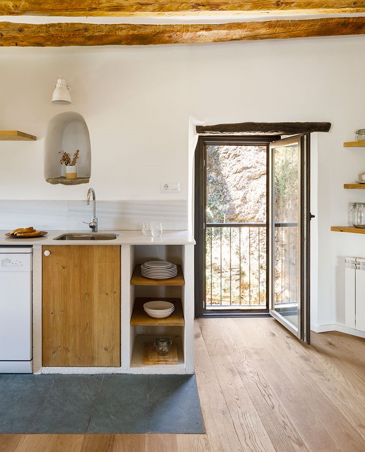 Detalle de cocina con estantes de madera, hornacinas en pared para detalles decorativos y apertura hacia exterior de vivienda