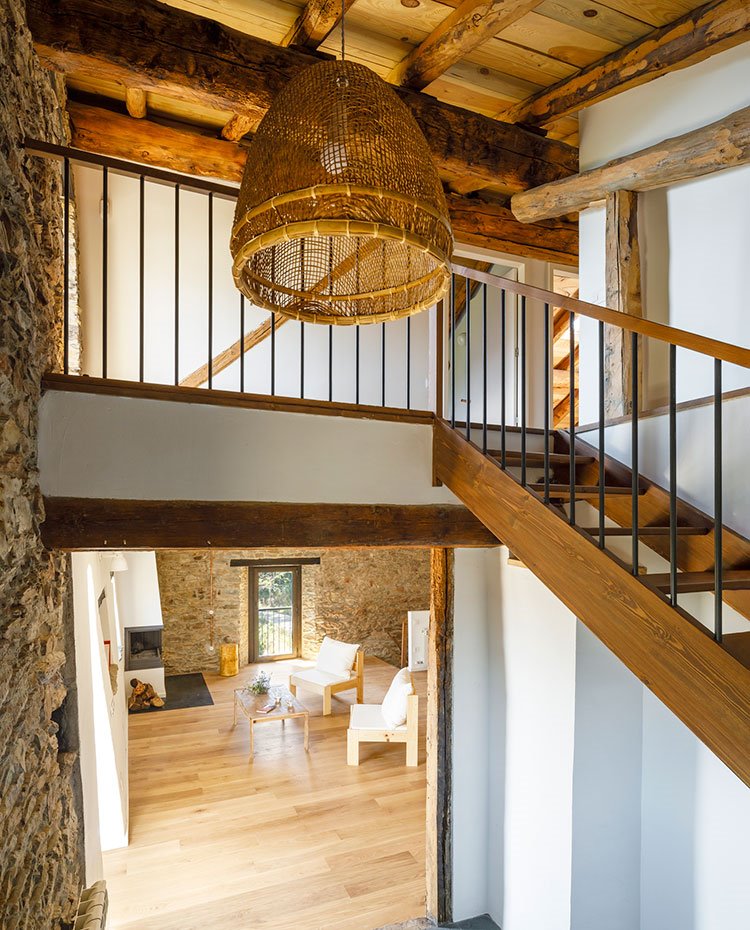 Detalle de sala de estar desde escalera hacia nivel superior, luminaria suspendida con pantalla de fibras naturales