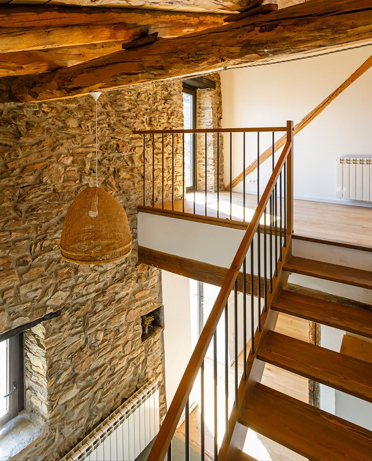 Escaleras entre dos de los niveles de la casa, peldaños de madera y barandilla con estrucutra de acero junto a pared de piedra vista