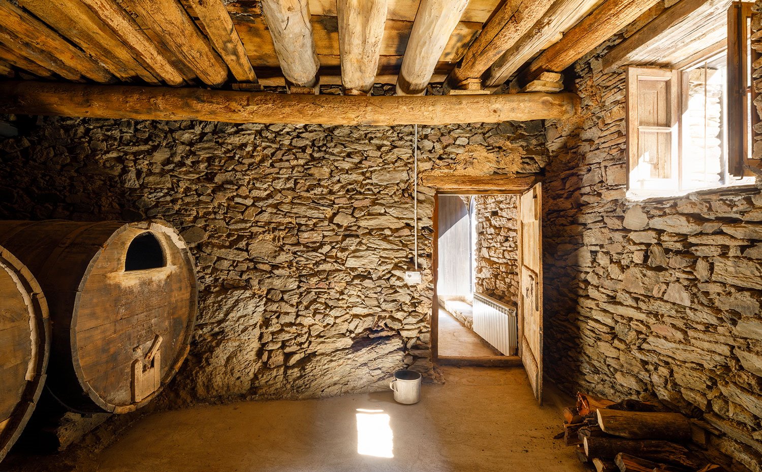 Interior habitación con paredes de piedra, vigas de madera en el techo y grandes tinajas antiguas