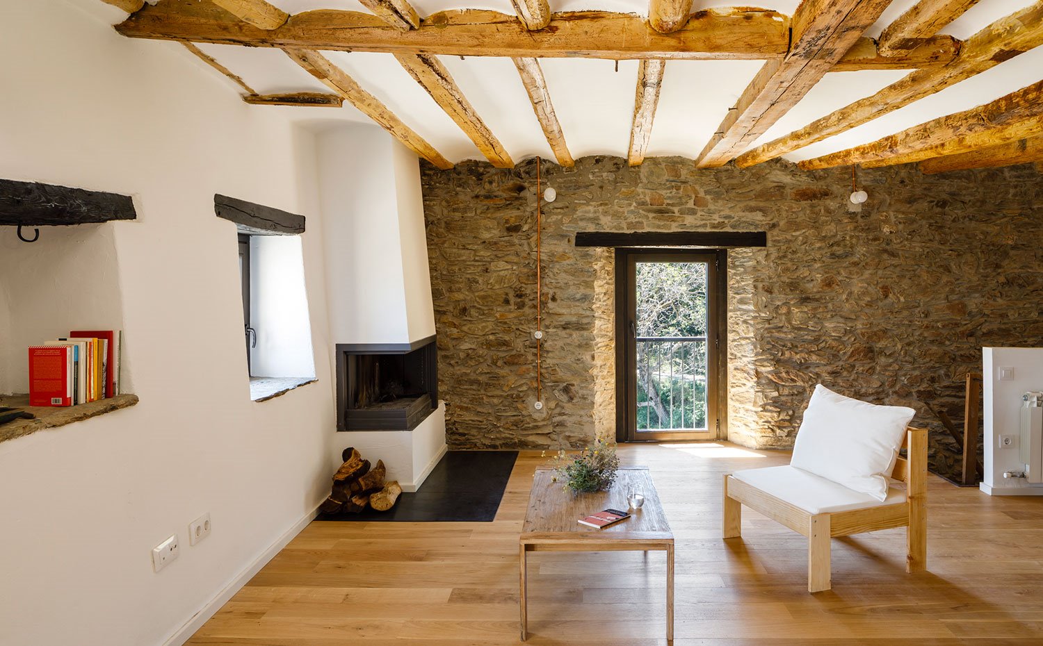 Salón con butaca y silla de madera, hornacinas en estructura rematadas con vigas de madera, chimenea oculta en estructura de obra