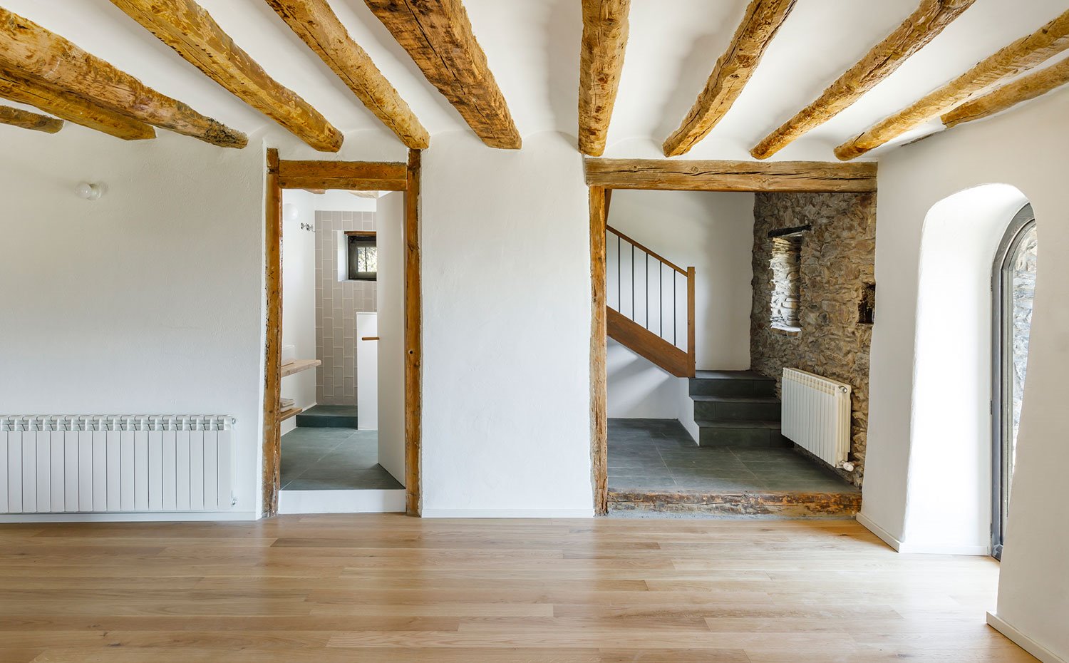 Zona diáfana con acceso a cuarto de baño y escaleras que conducen a nivel superior, con marcos de madera y vigas en el techo