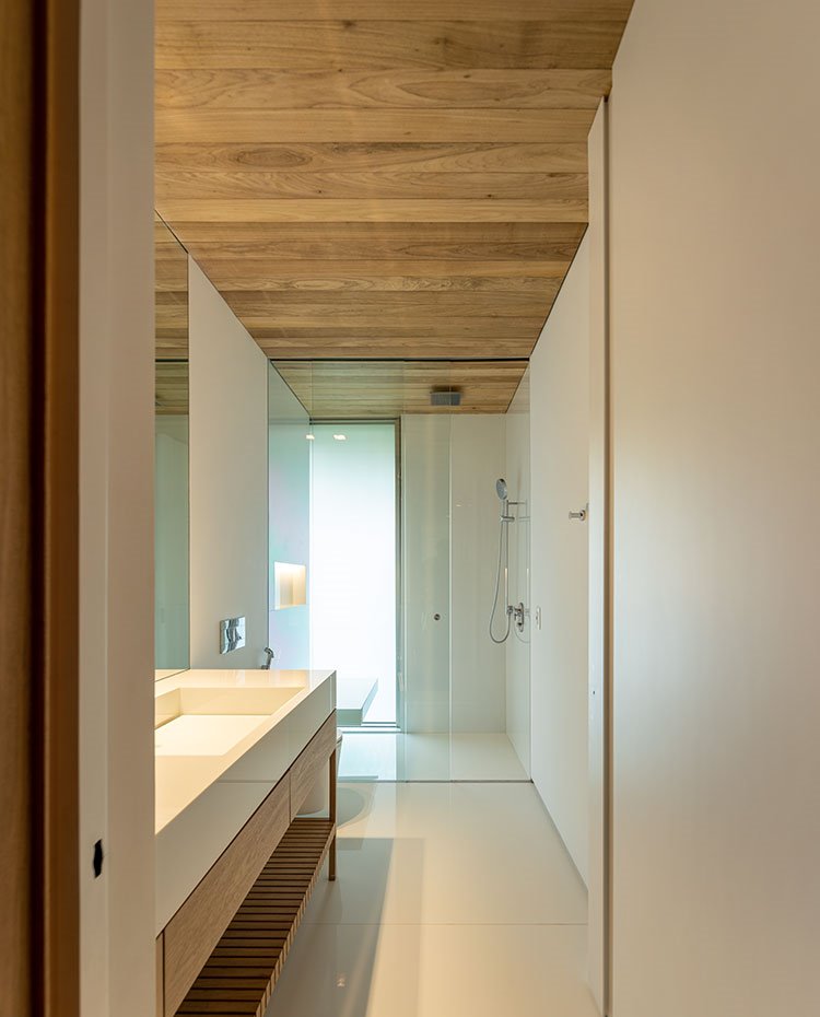 Cuarto de baño con techos y mobiliario en madera, encimera en blanco, ducha con cerramientos acristalados