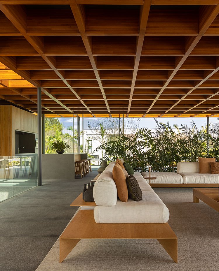 Salón desde lateral con mesas y asientos con estructura de madera y cocina al fondo con isla de trabajo y office