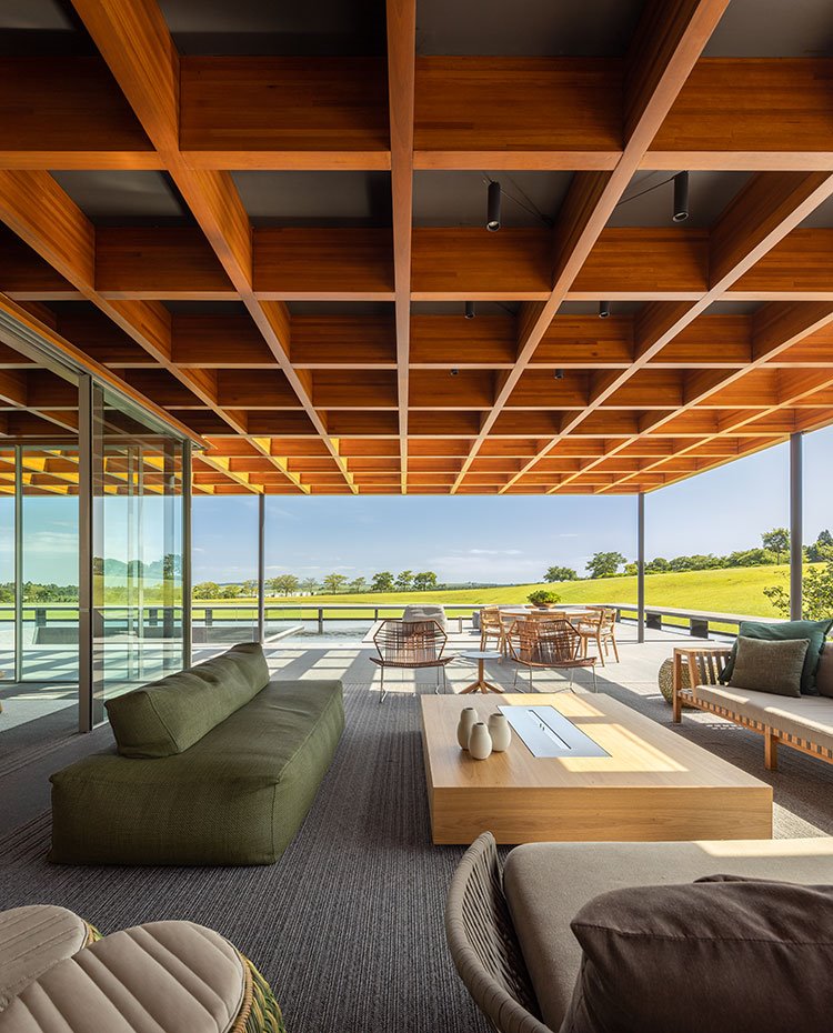 Salón exterior con chimenea, sofás verdes y tonos tierra, cubierta a modo de celosía cuadriculada