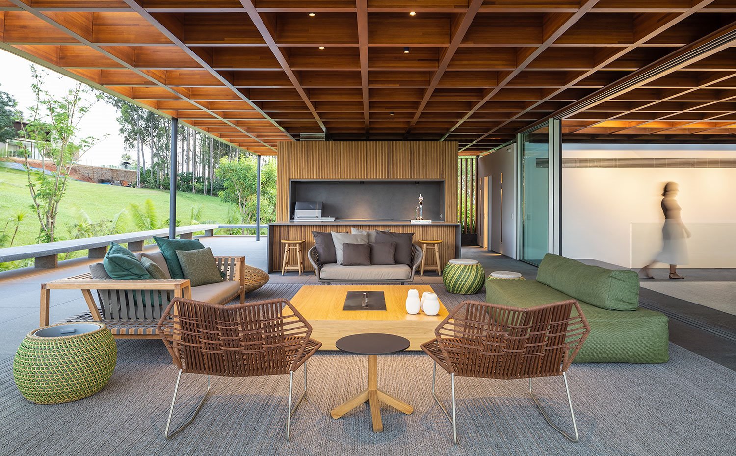 Salón y zona de barbacoa cubierta con butacas marrones y sofás en verde y marrón, mobiliario en acabado madera