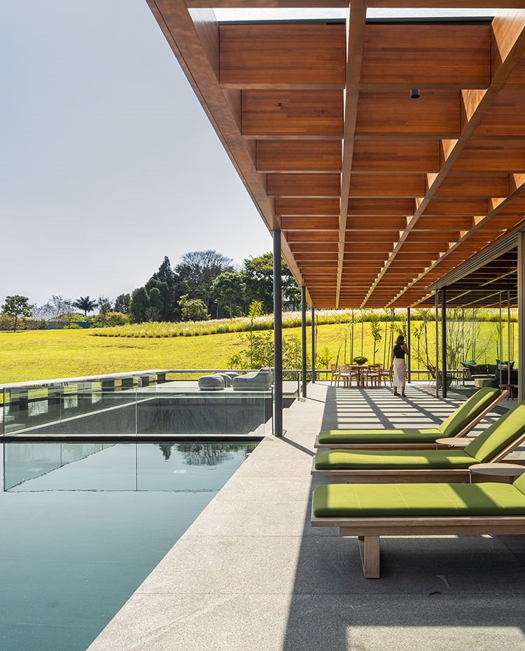 Tumbonas en madera y tapizadas en verde junto a piscina bajo cubierta a modo de celosía