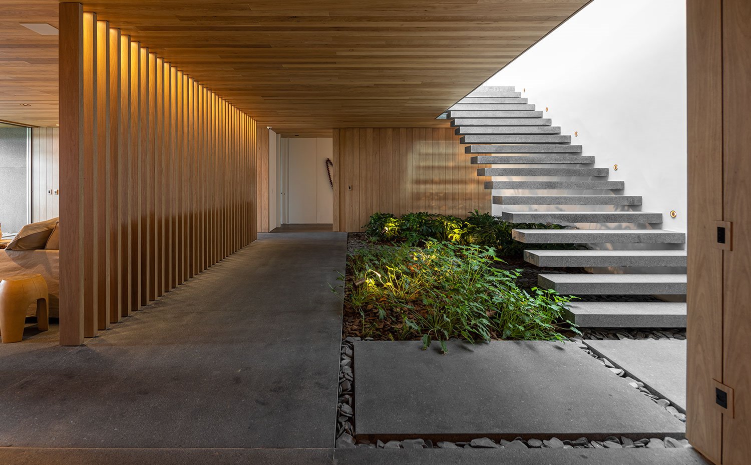Zona de paso con jardín interior bajo escaleras en voladizo con revestimiento en madera