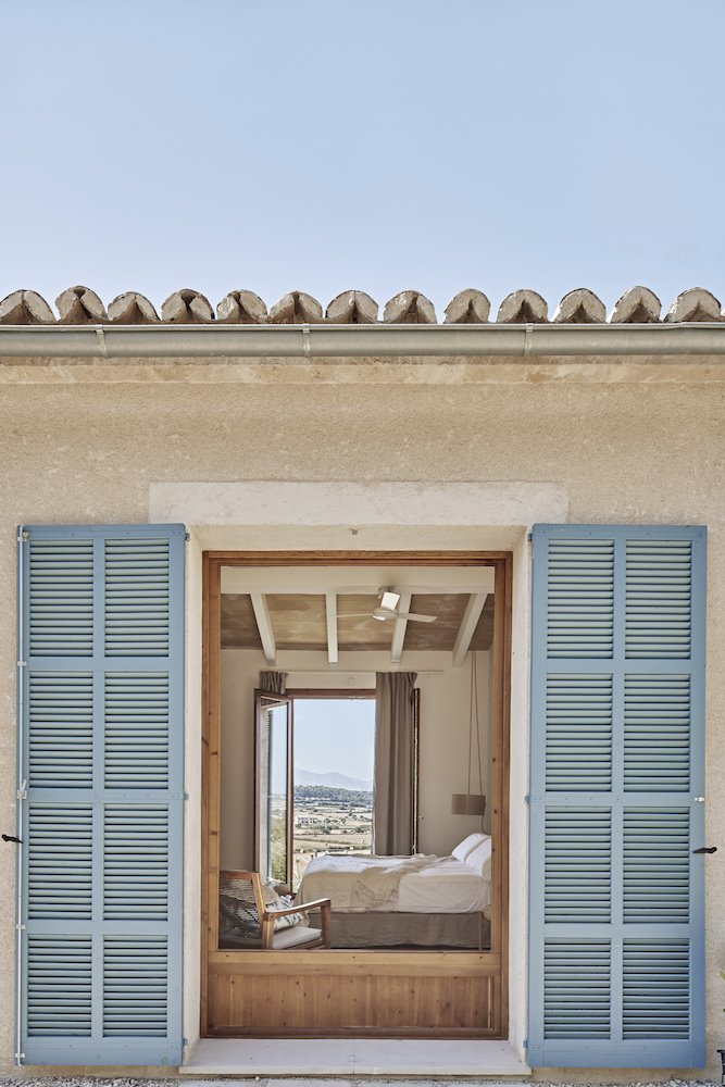 Ventana del dormitorio con porticones azules de una Casa en Mallorca del estudio de arquitectura OHLAB