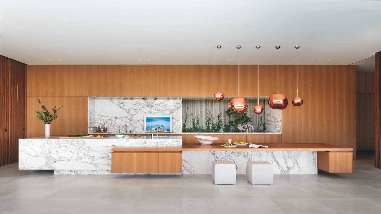 Cocina con isla de marmol y paredes de madera lamparas de cobre suspendidas