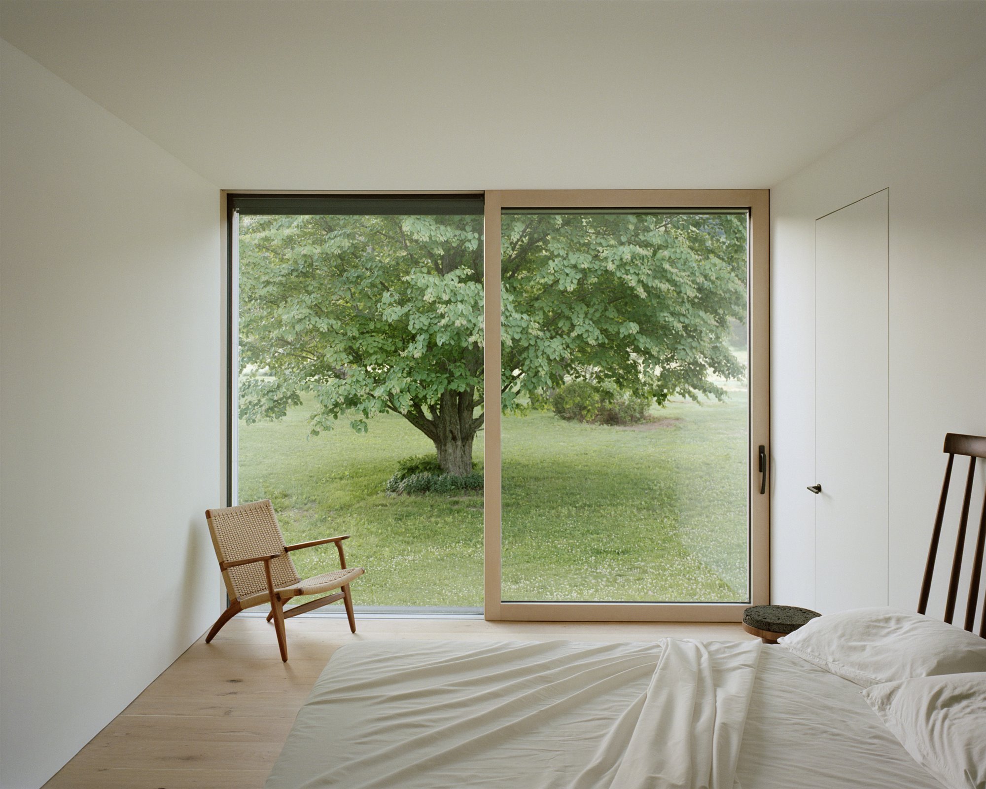 Dormitorio abierto al jardin con silla de madera y puertas de cristal