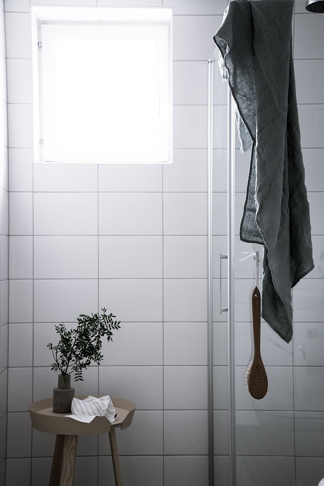 Baño con baldosas cuadradas blancas y taburete de madera