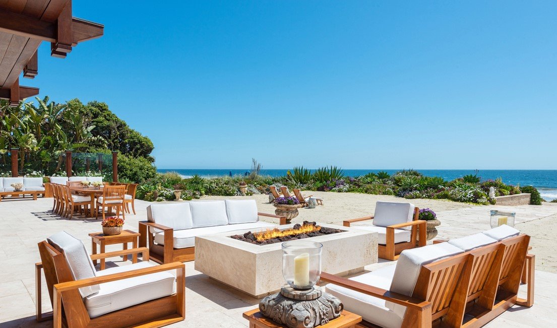 salon exterior con sillas de teca y chimenea estufa  de la casa de pierce brosnan
