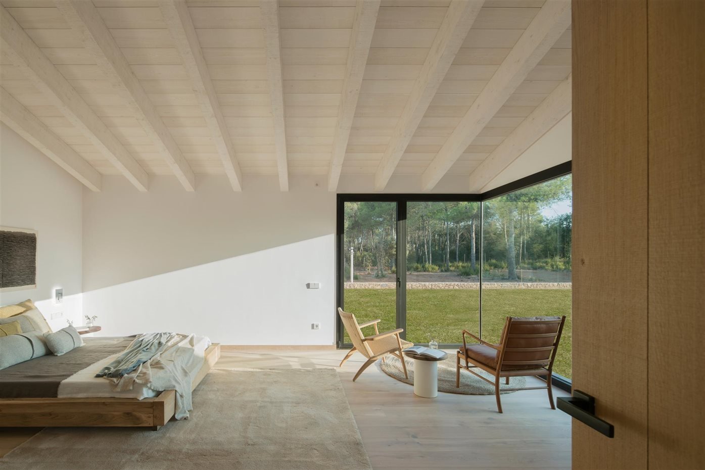 Dormitorio con vigas de madera de color blanco y butacas junto a una ventana