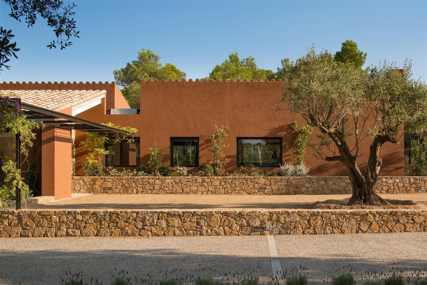 Fachada de una casa de color terracota con un olivo