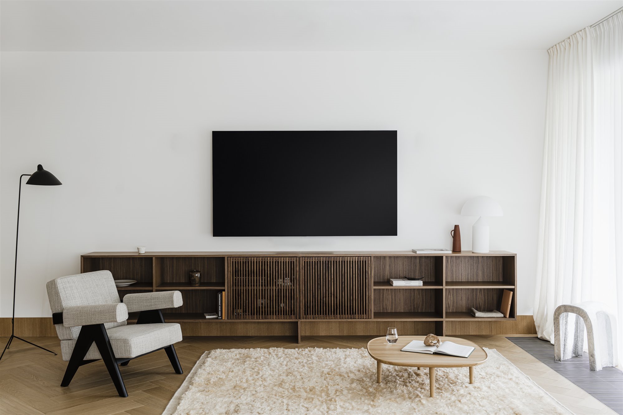 Salon con mueble de madera bajo la televisión y alfombra blanca