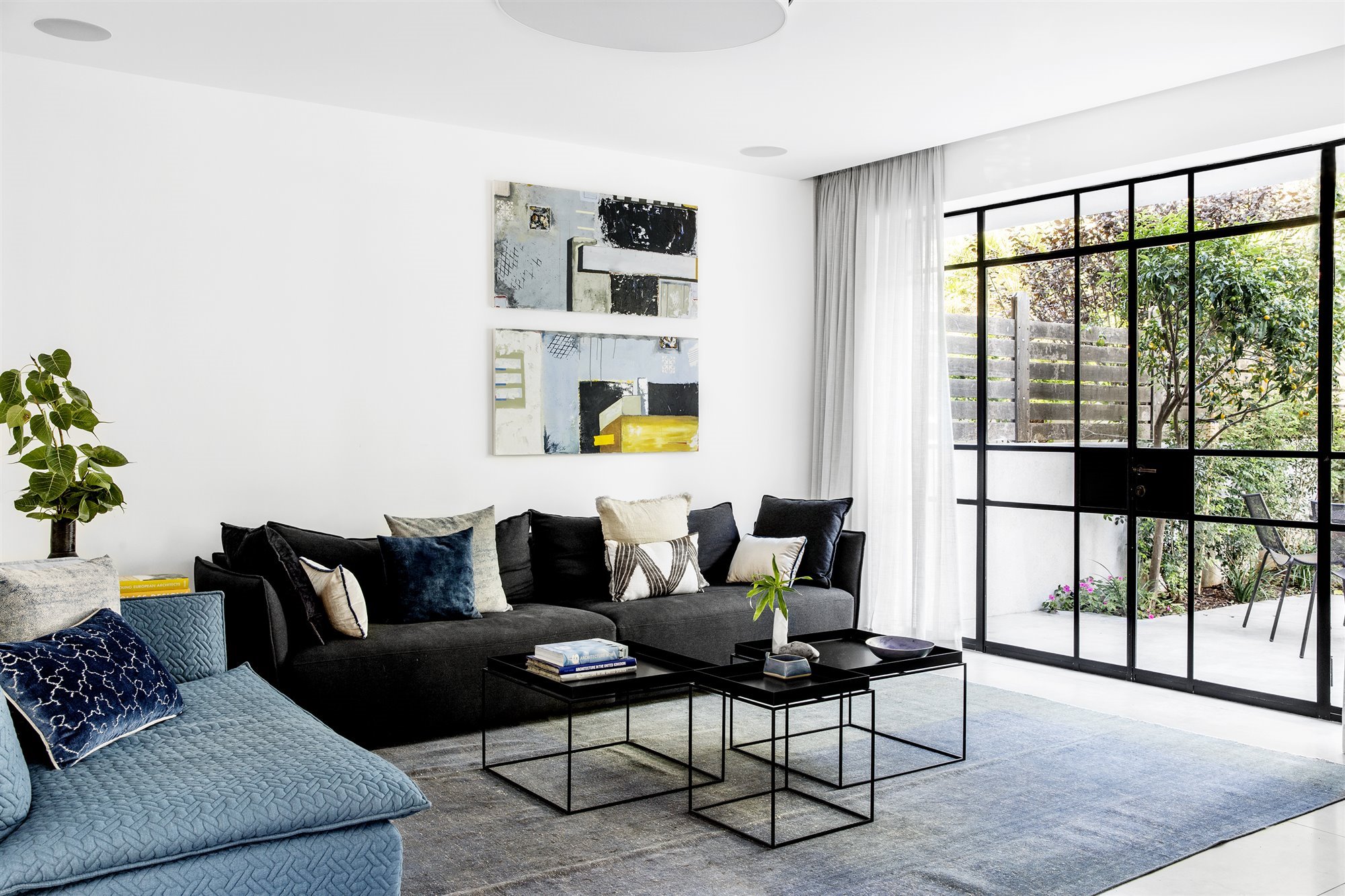 salon de una casa con sofa de terciopelo negro y mesillas auxiliares