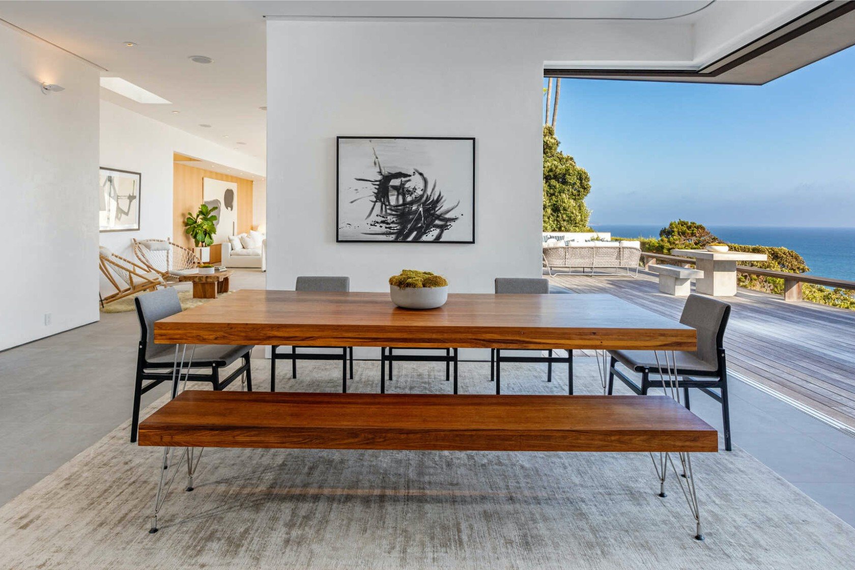 Comedor con banco de madera y sillas de color gris abierta con vistas al mar