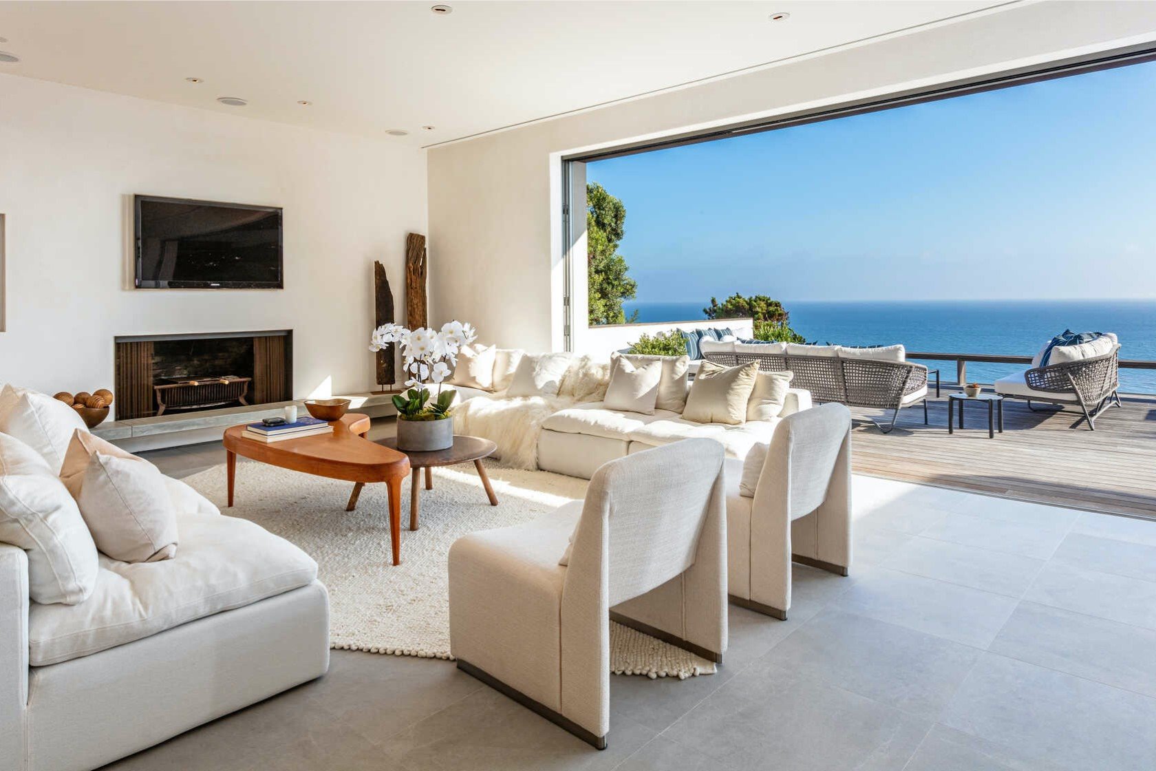 salon con sofas y butacas de color blanco chimenea y mesillas auxiliares de madera abierto con vistas a la playa