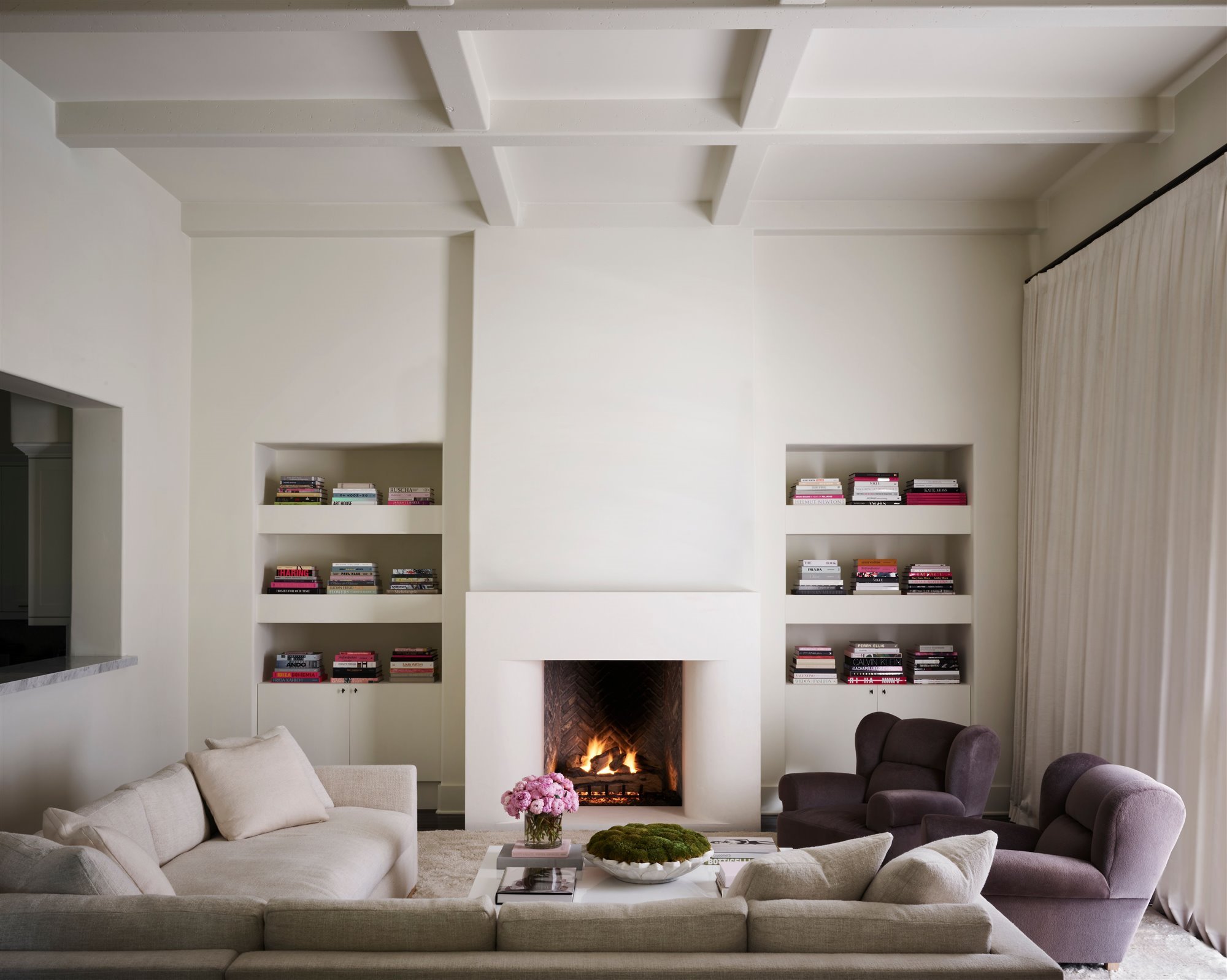 Salon con chimenea y techo con vigas de color blanco sillones lilas y sofa blanco de la casa Kourtney Kardashian en Calabasas