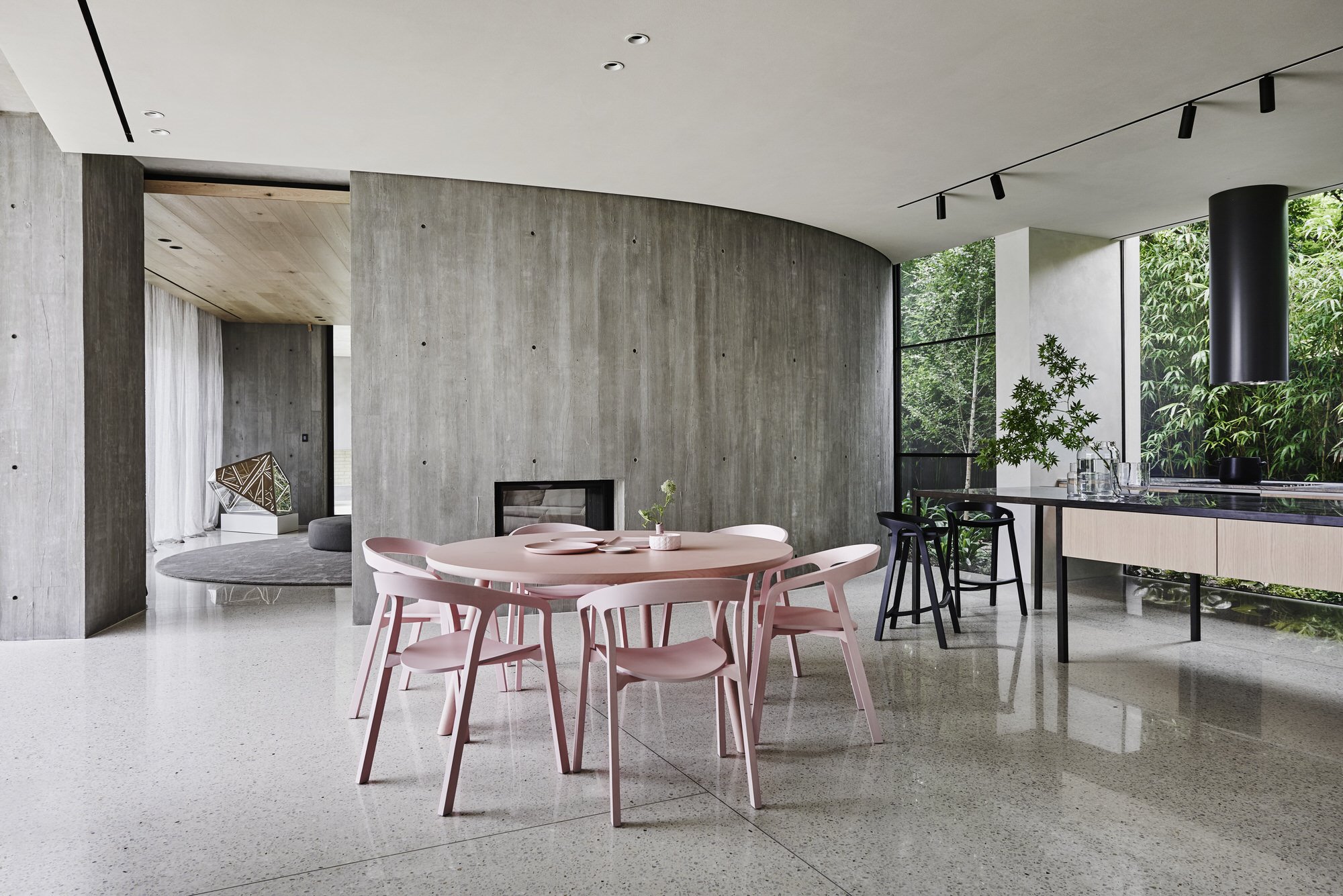 Comedor con sillas y mesa de color rosa y paredes de hormigón de una casa en Australia