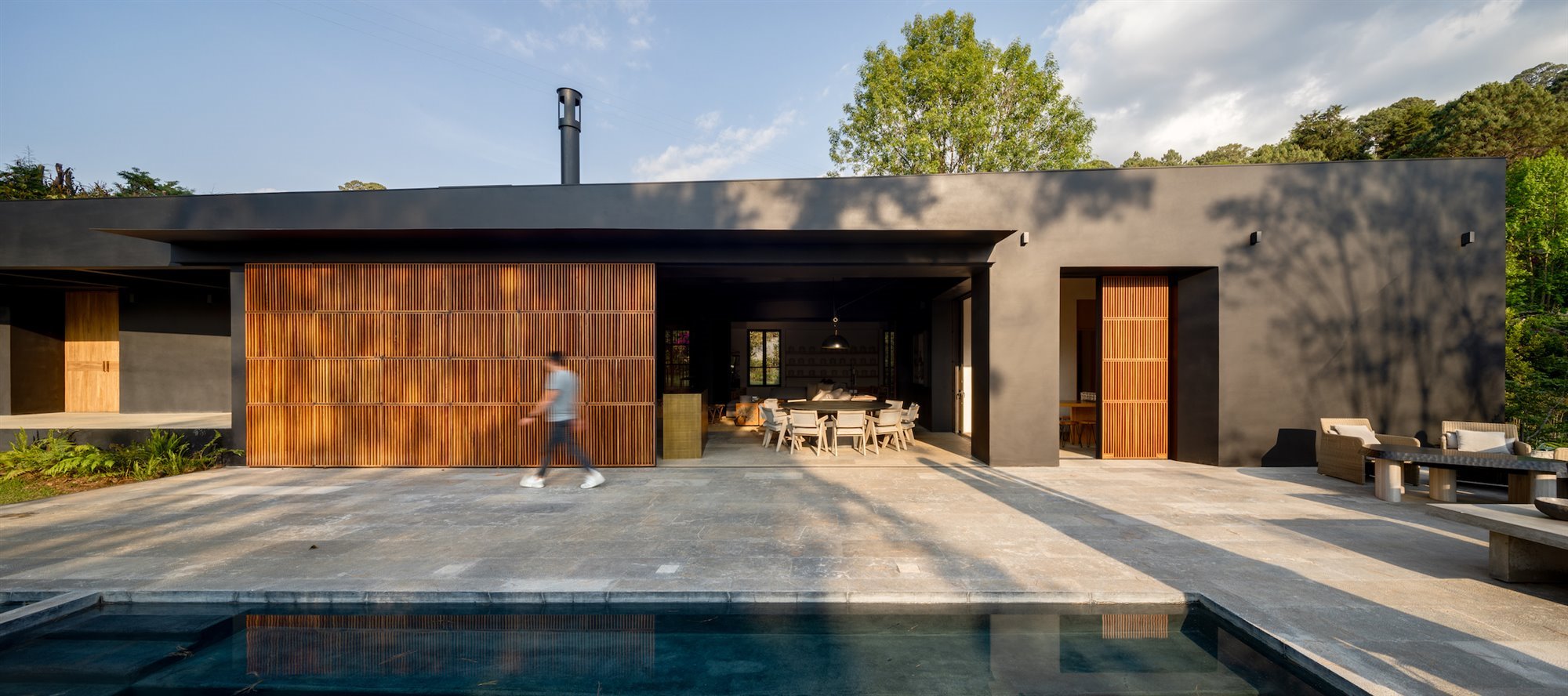 Casa con fachada de color negro y pared de madera tipo celosia