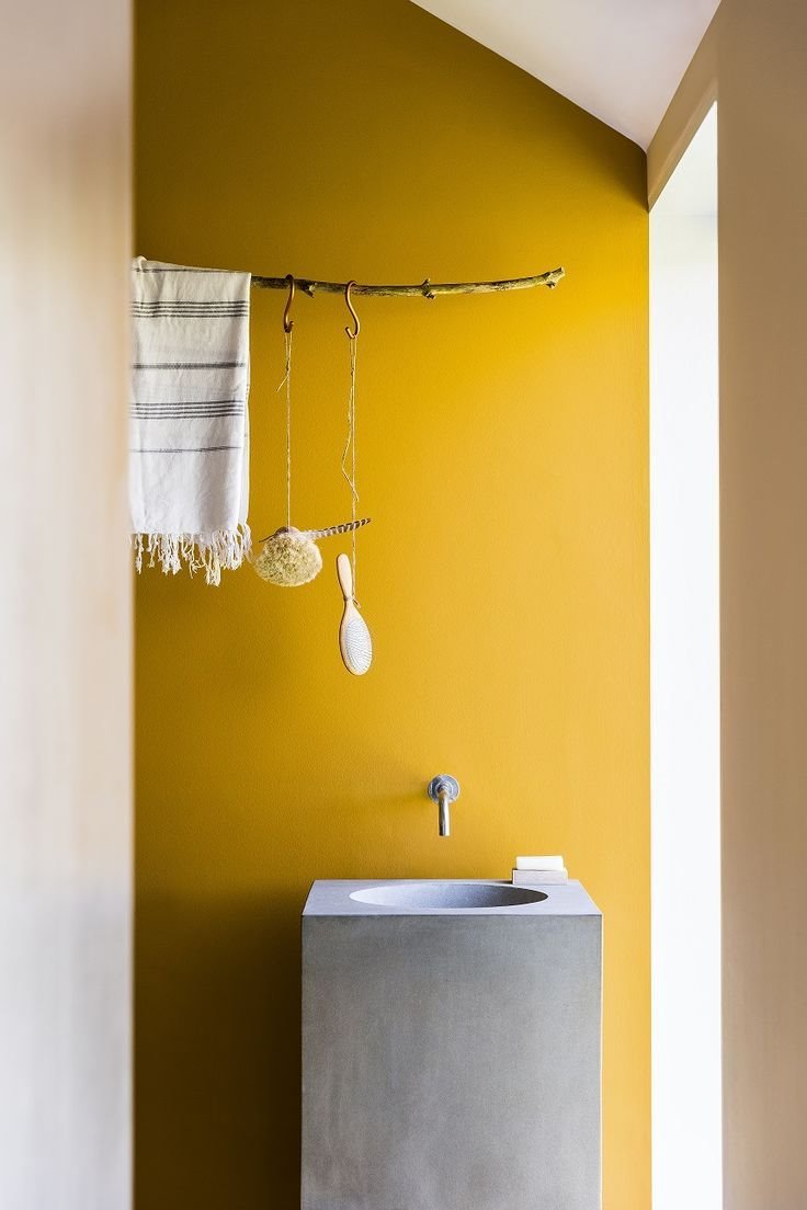 Baño con paredes de color amarillo y lavamanos de cemento gris