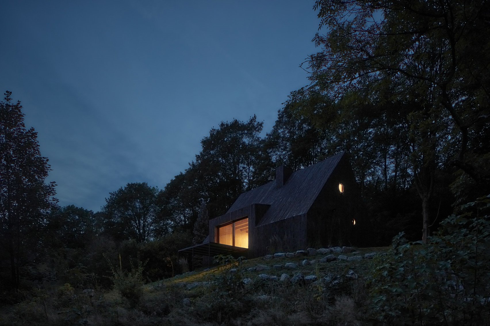 Casita de madera negra en el bosque con luces encendidas de noche