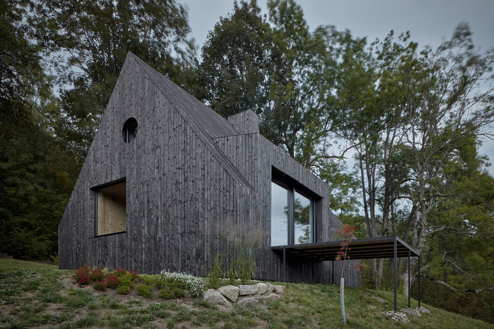 Casita de madera negra en el bosque con porche