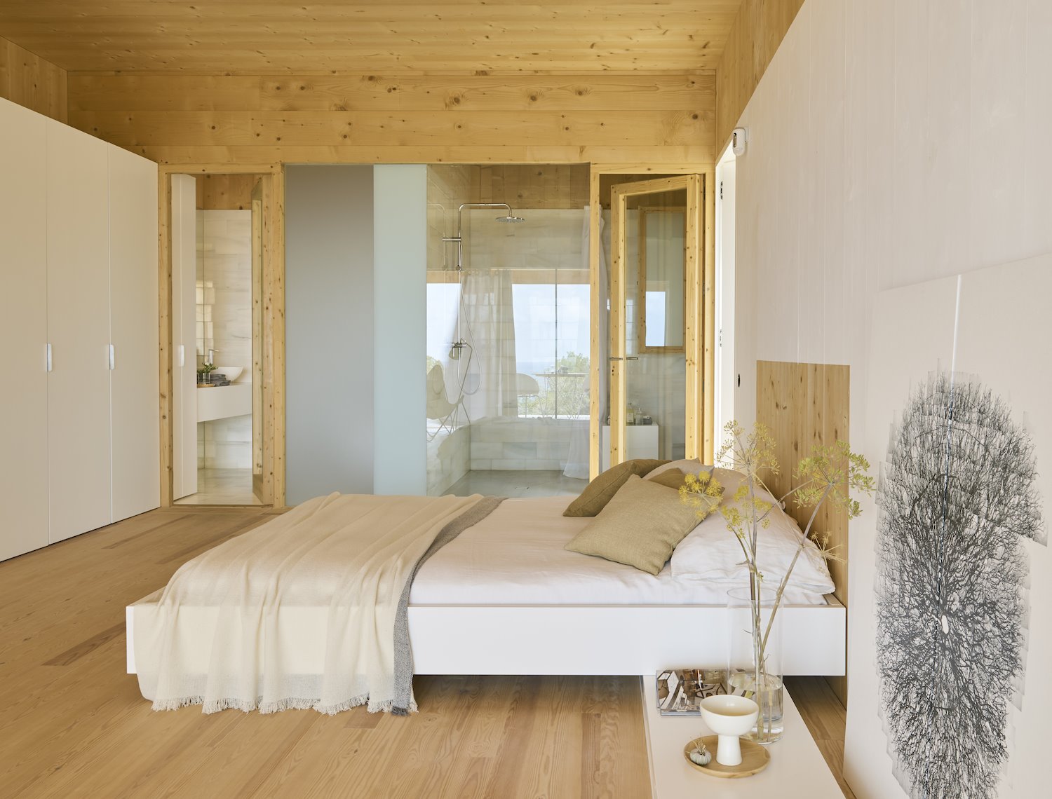 Dormitorio de una casa en madera natural con sabanas de lino y puertas de cristal